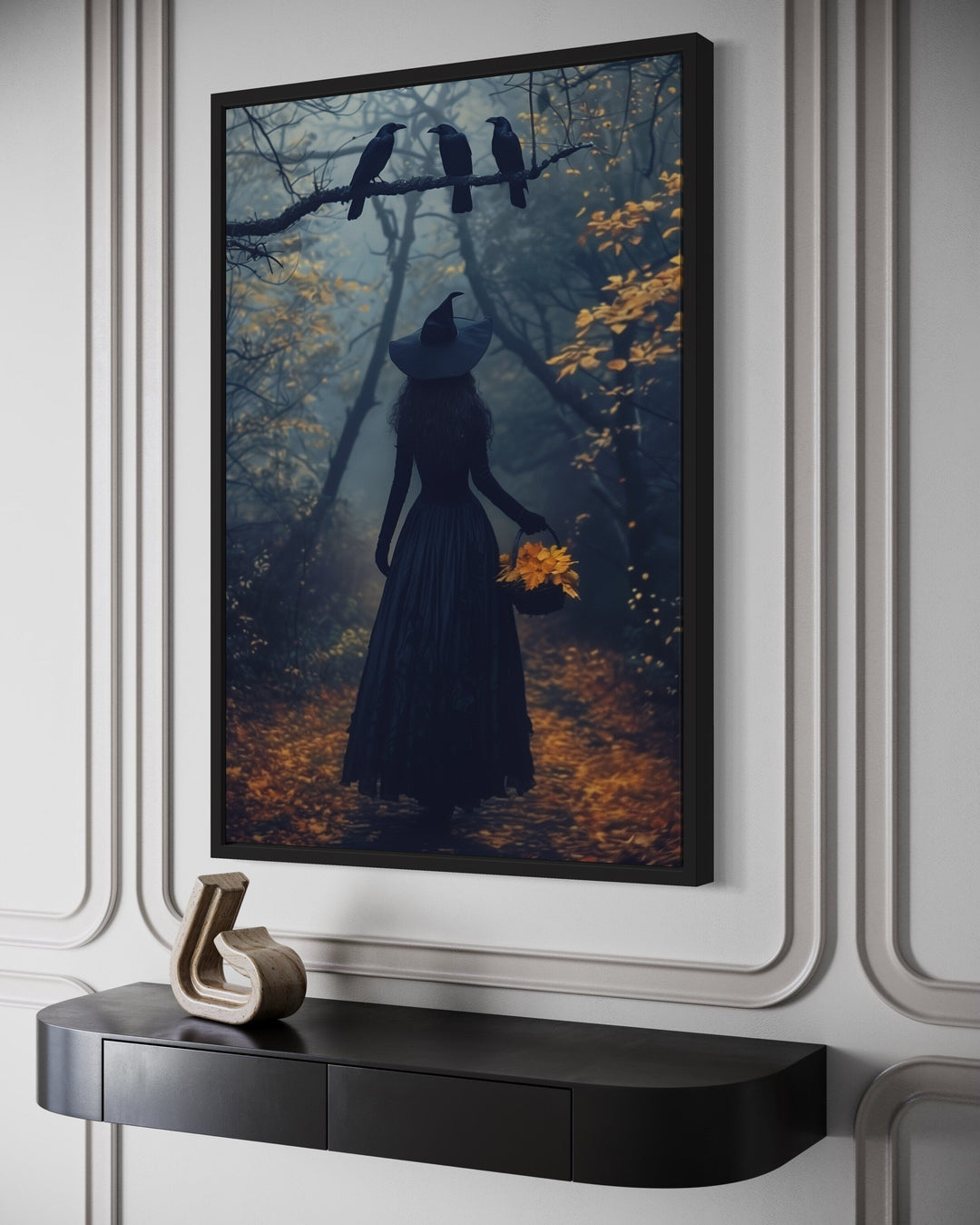 Framed wall art of a witch in a dark autumn forest with ravens, displayed above a black console.