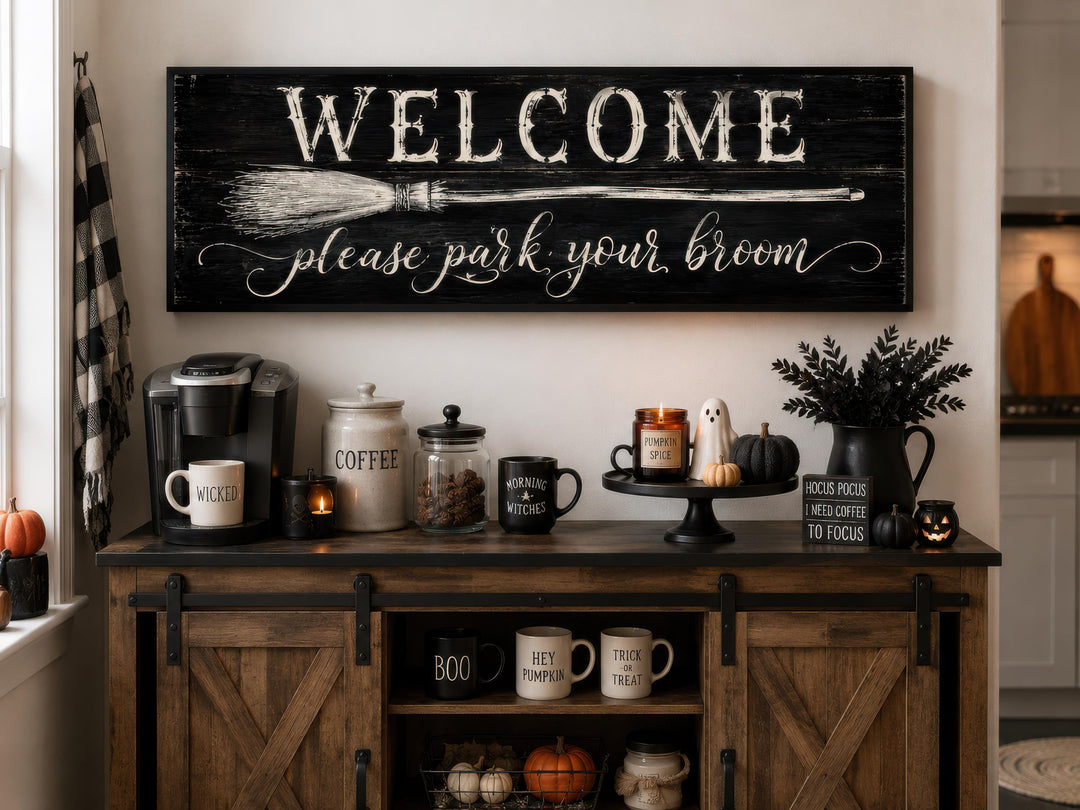 Horizontal black wood sign with white text reading 'WELCOME please park your broom' above a coffee bar.