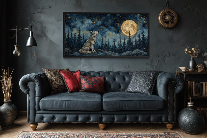 A framed canvas print of a wolf under a full moon hangs above a dark tufted sofa in a moody room.
