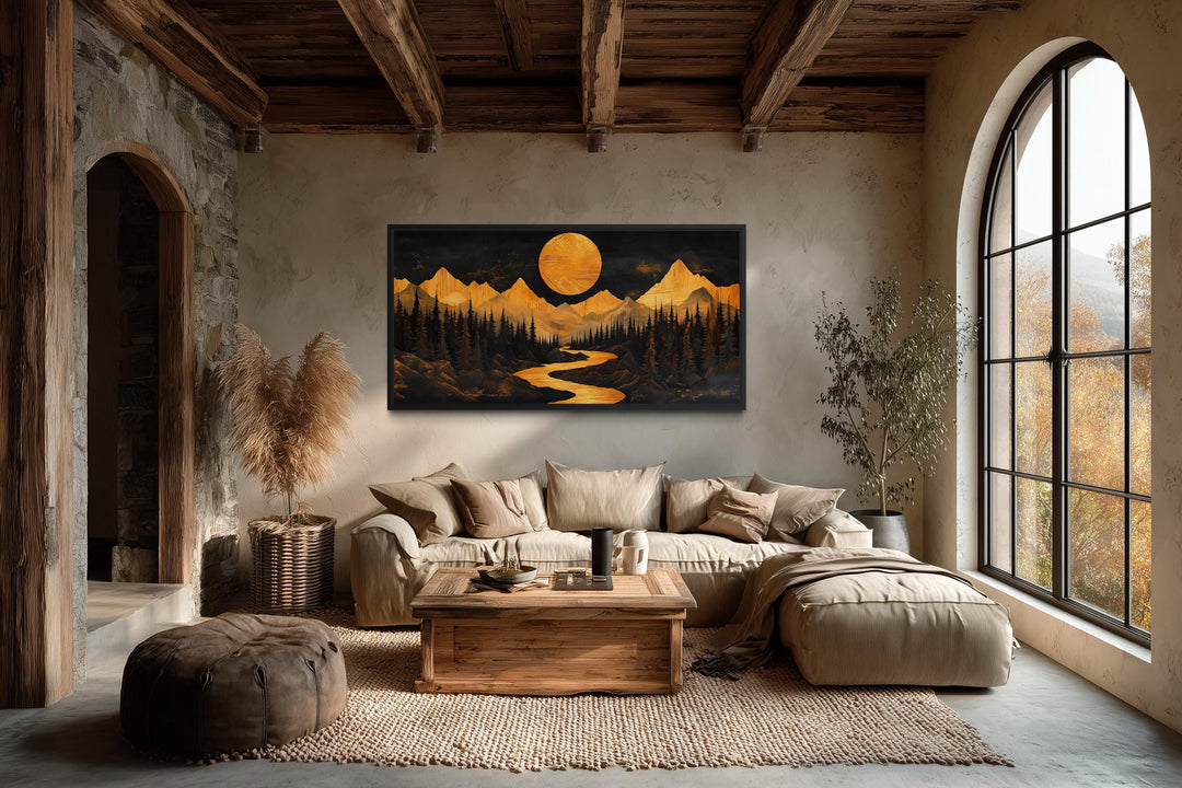 Framed canvas wall art of a golden mountain river and moon in a rustic cabin living room.