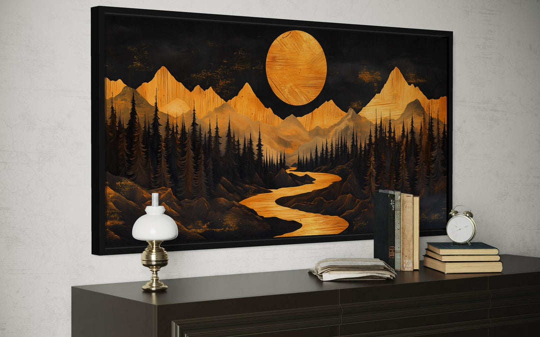 Framed canvas wall art of a golden mountain river and moon landscape above a dark wood dresser.