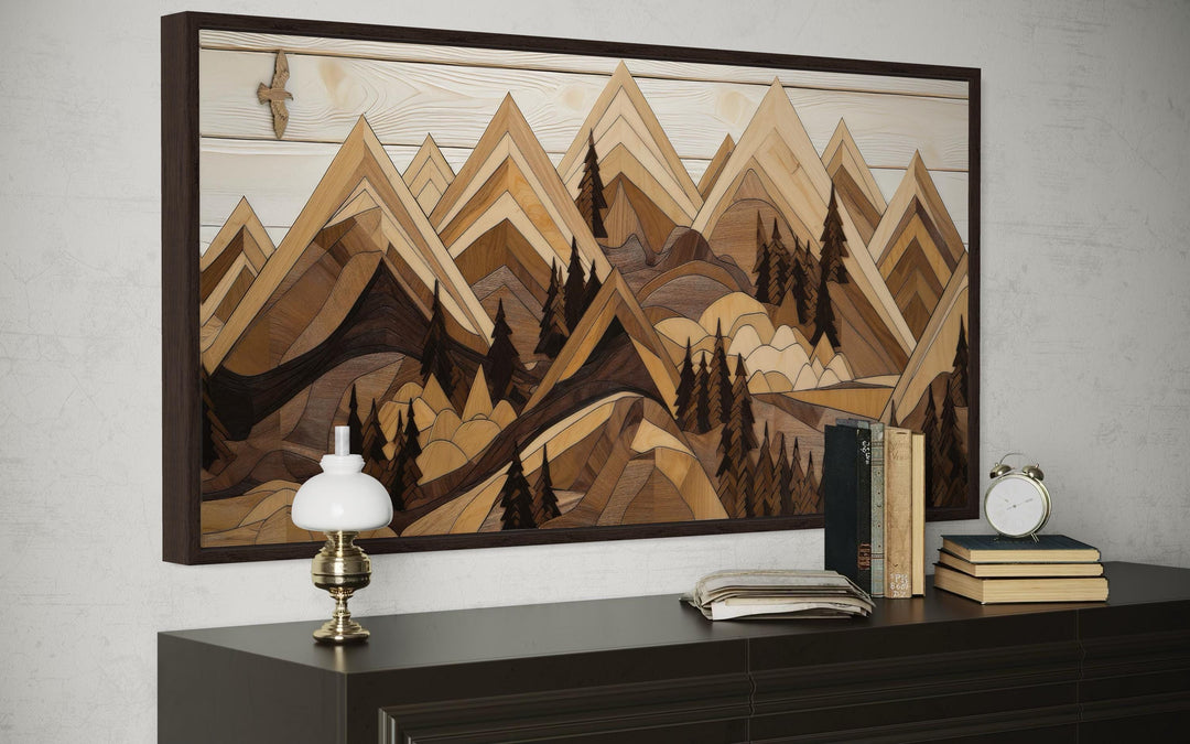 Wooden mountain with eagle framed canvas wall art above a dark dresser with books and a lamp.