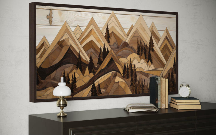 Wooden mountain with eagle framed canvas wall art above a dark dresser with books and a lamp.