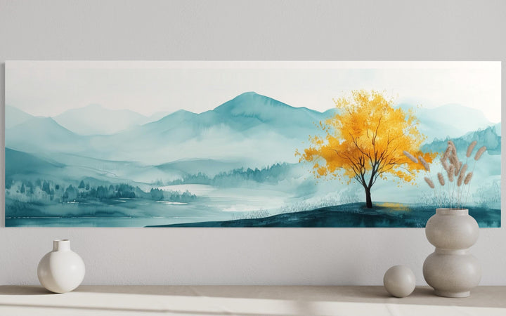Long horizontal wall art of a golden yellow tree against a misty teal mountain landscape.