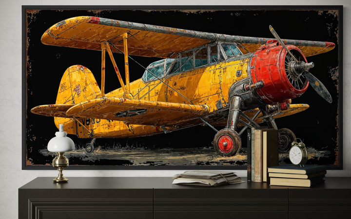Yellow vintage biplane framed canvas wall art displayed above a dark dresser with books and a lamp.