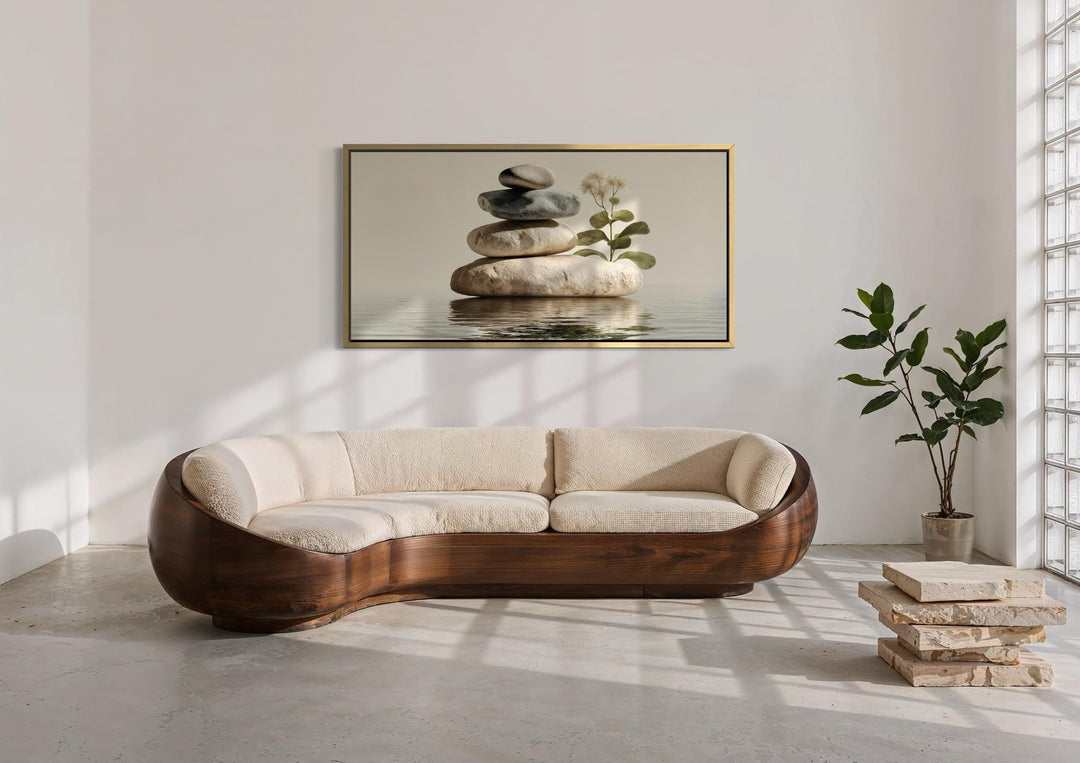 Horizontal wall art of stacked stones and a plant above a curved wood sofa in a minimalist room.