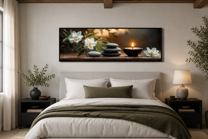Zen stones, candle, and magnolia flowers on a long horizontal framed canvas above a bed.