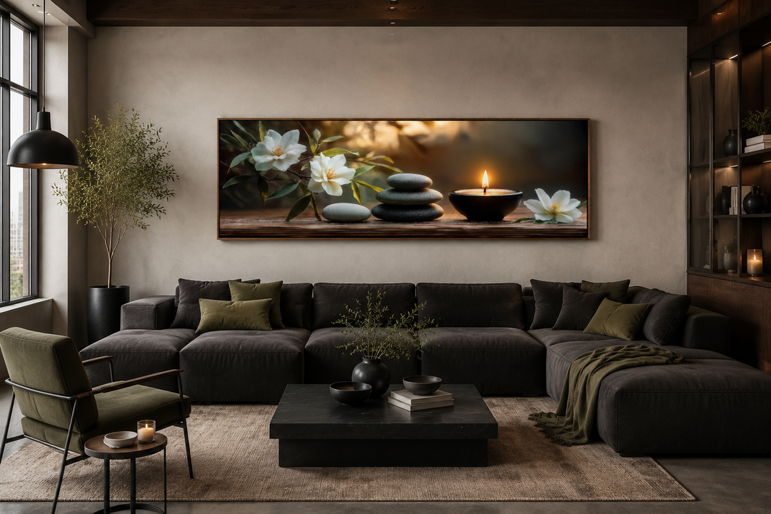 Zen stones, candle, and magnolia flowers on a long horizontal framed canvas above a dark sofa.