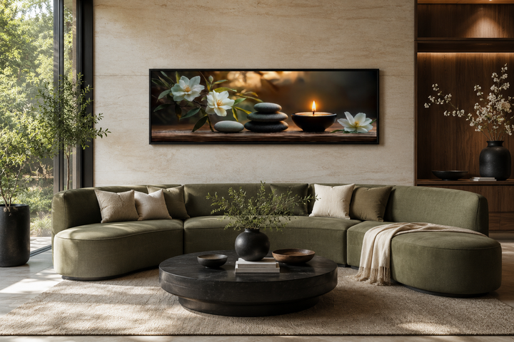 Zen stones, candle, and magnolia flowers on a long horizontal framed canvas above a green sofa.