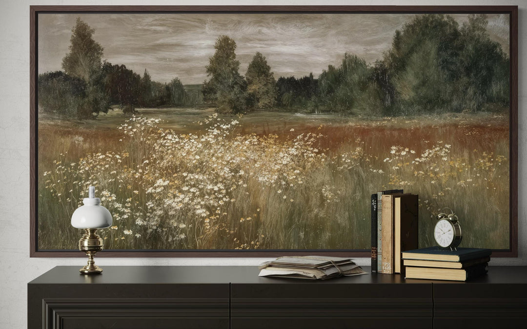 A framed canvas print of a neutral wildflower meadow landscape above a dark wooden dresser.
