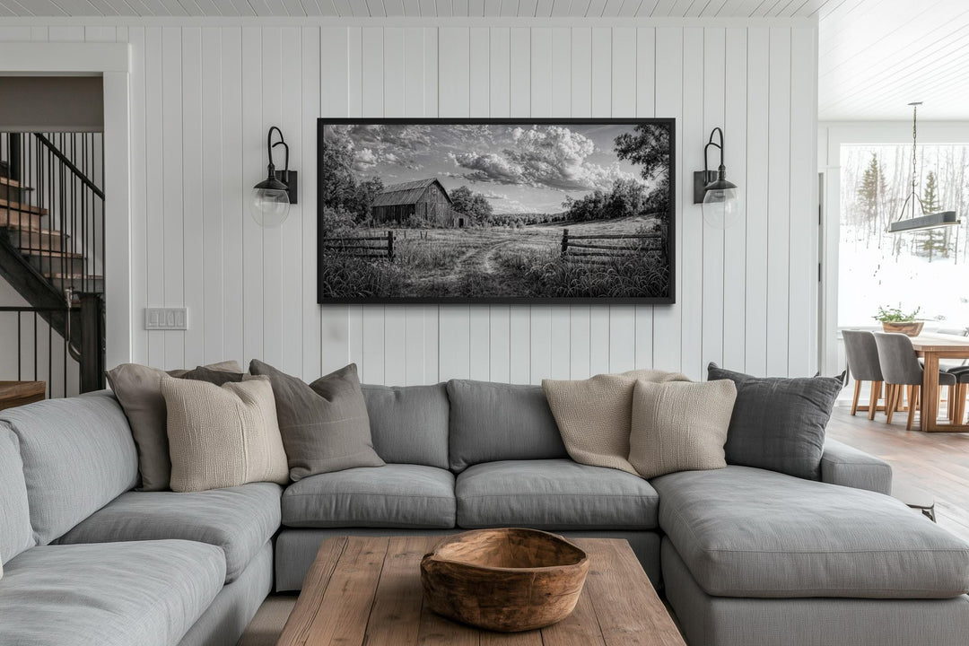 Black and white barn landscape canvas wall art hanging above a gray sectional sofa in a living room.