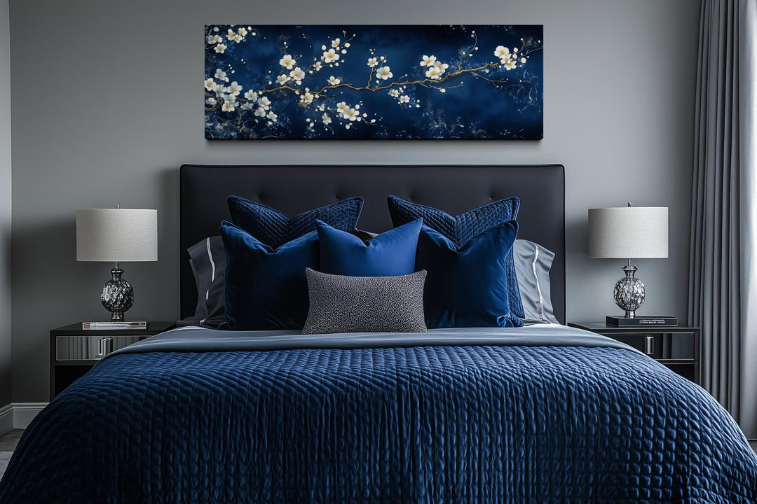 Panoramic cherry blossom canvas print on navy blue hanging above a modern bed with blue bedding.