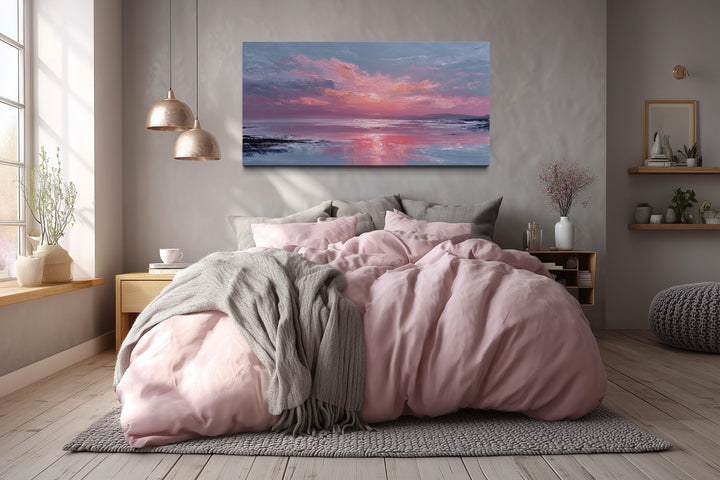 A blush pink ocean sunset canvas wall art hangs above a bed with matching pink and grey bedding.