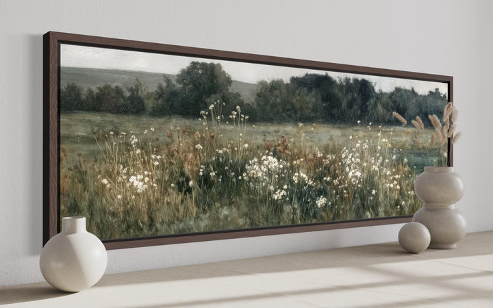A long, narrow horizontal painting of a moody wildflower field in a dark wood frame.