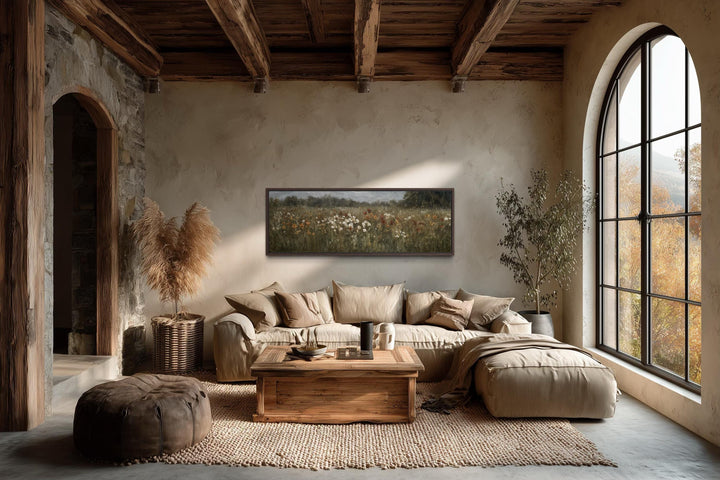 A long horizontal canvas of a moody wildflower field hangs above a sofa in a rustic living room.