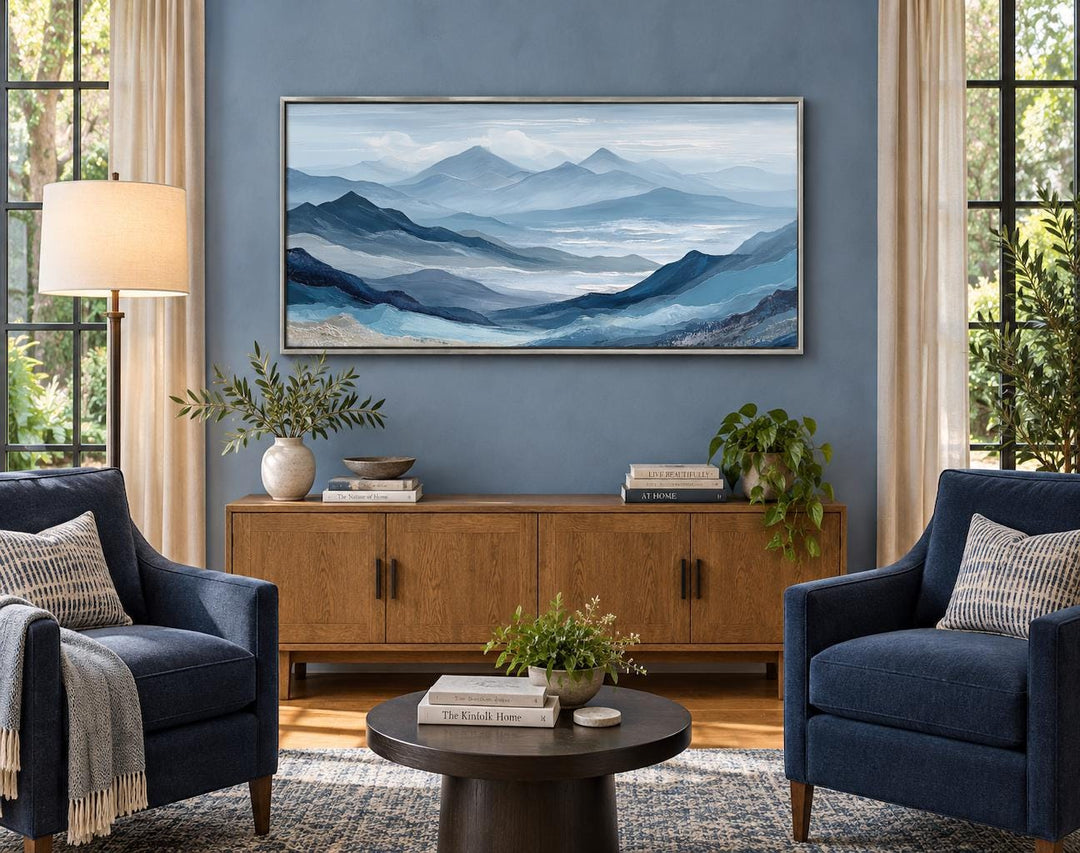 Blue mountain landscape canvas wall art with misty peaks above a wooden console in a living room.
