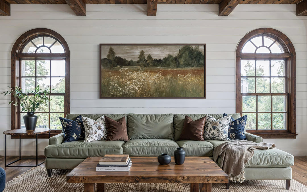 A framed canvas print of a neutral wildflower meadow landscape hangs above a green sofa.