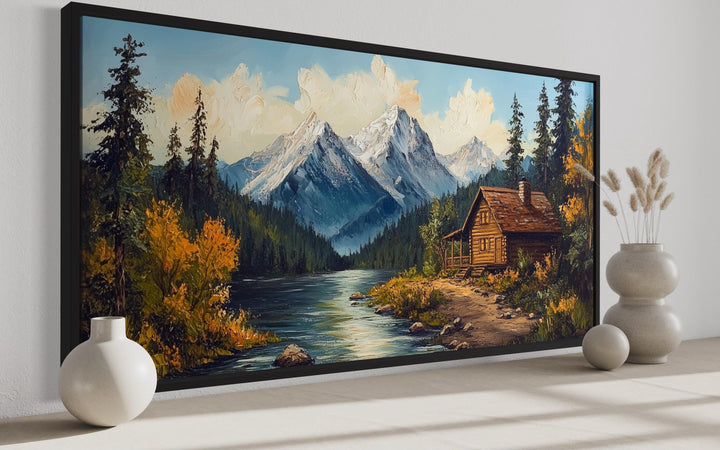 Vintage style canvas wall art of a log cabin by a river with snow-capped mountains in the background.