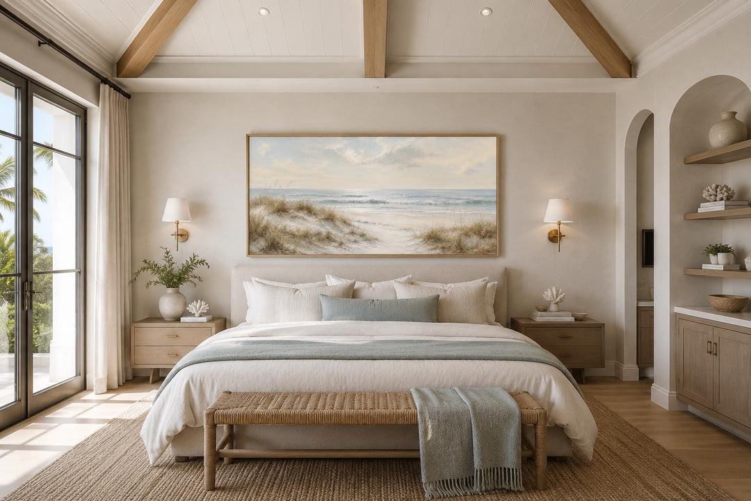 Wide horizontal wall art of sandy beach dunes and rolling waves in a slim gold frame above a bed.
