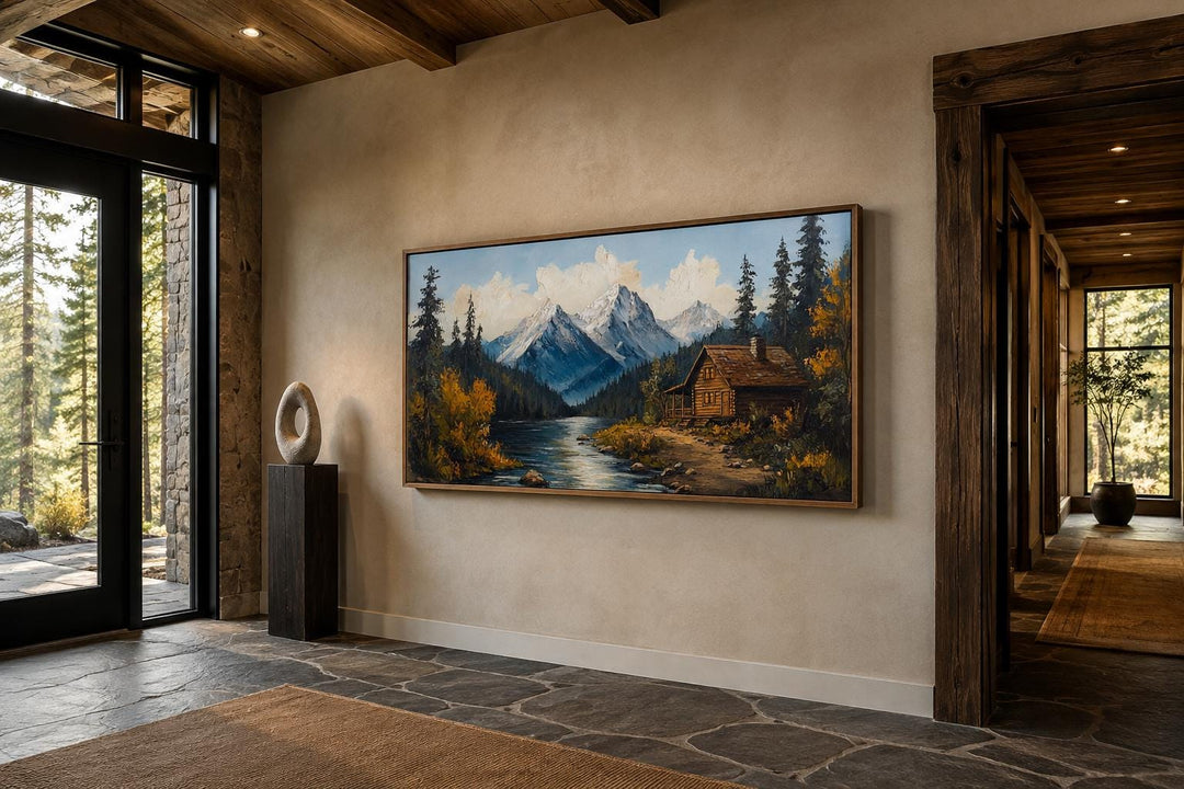 Vintage style canvas wall art of a mountain cabin by a river in a rustic home interior.