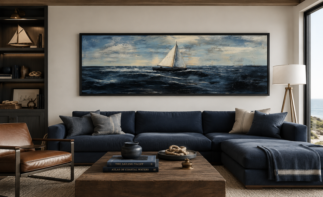 Long horizontal nautical wall art of a sailboat on a dark blue ocean above a navy sectional sofa.